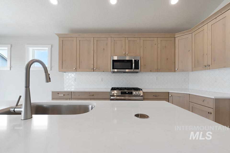 Kitchen with stainless steel appliances, light countertops, decorative backsplash, recessed lighting, and light brown cabinets
