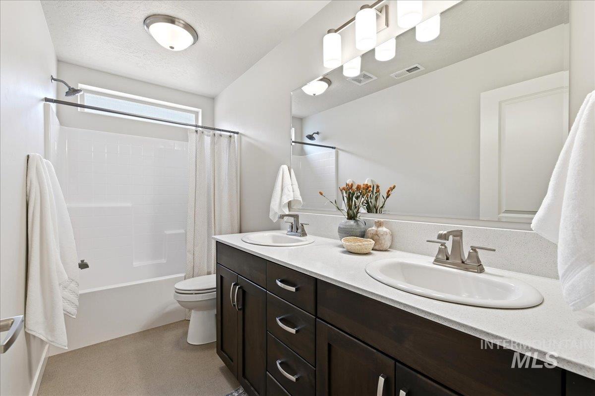 Bathroom featuring a dual-sink vanity with dark wood-finish cabinetry, light-toned countertop, and brushed nickel hardware