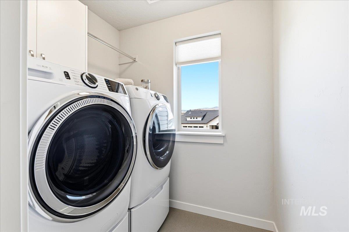 Dedicated laundry area featuring front-loading appliances, overhead cabinetry, a clothing rod, and a window providing natural illumination