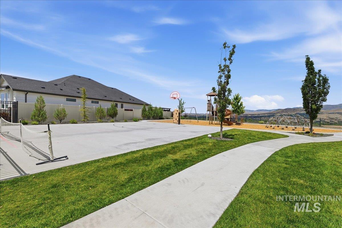 Expansive outdoor recreation area featuring a paved sports court with a basketball hoop and tennis net, a dedicated playground with swings and a climbing dome, and a winding concrete pathway