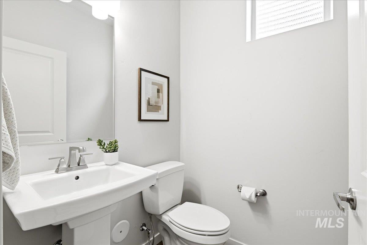 Pedestal sink with chrome faucet and mirror, complemented by a white toilet and a high-set window