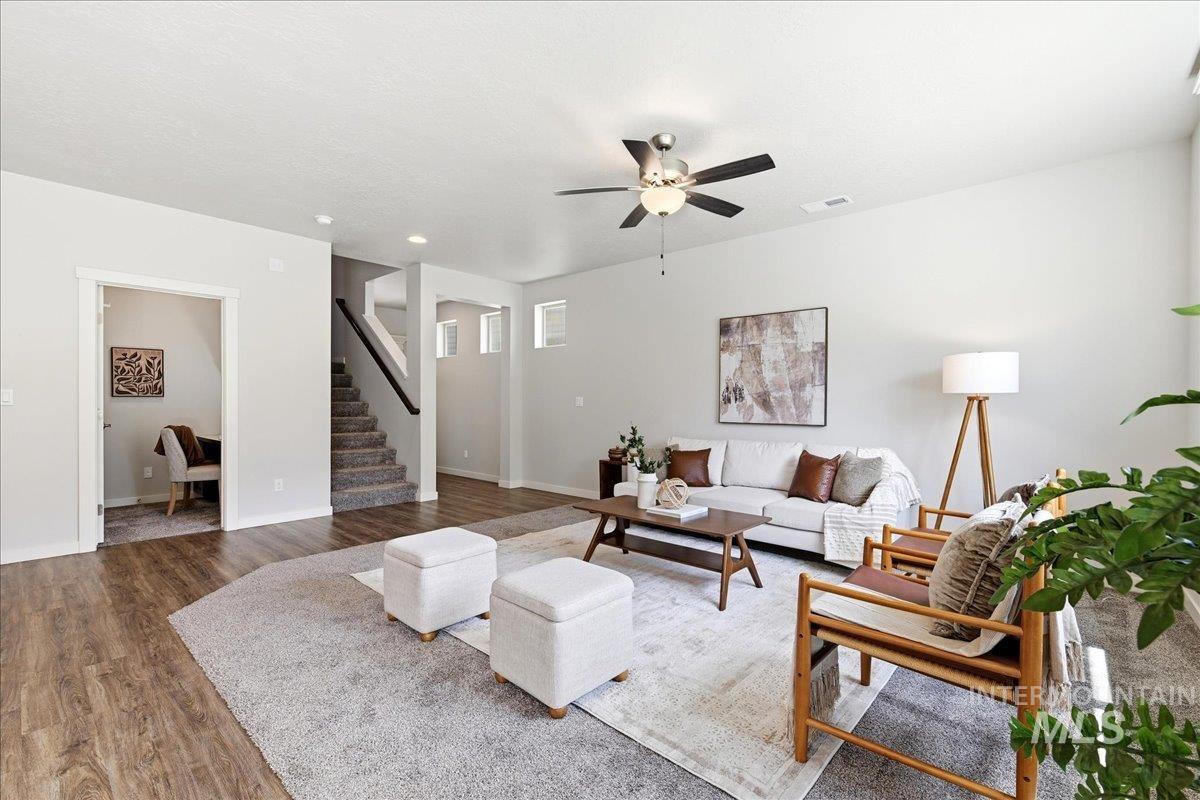 Spacious living area featuring wood-finish flooring, a ceiling fan with integrated lighting, and neutral wall tones