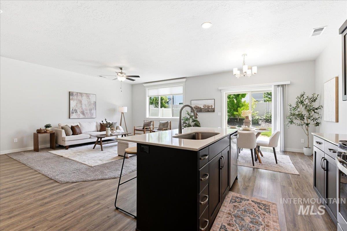 Open-concept interior featuring wood-finish flooring, a kitchen island with sink and light-toned countertop, a dining area with direct access to the exterior, and a living area with a ceiling fan