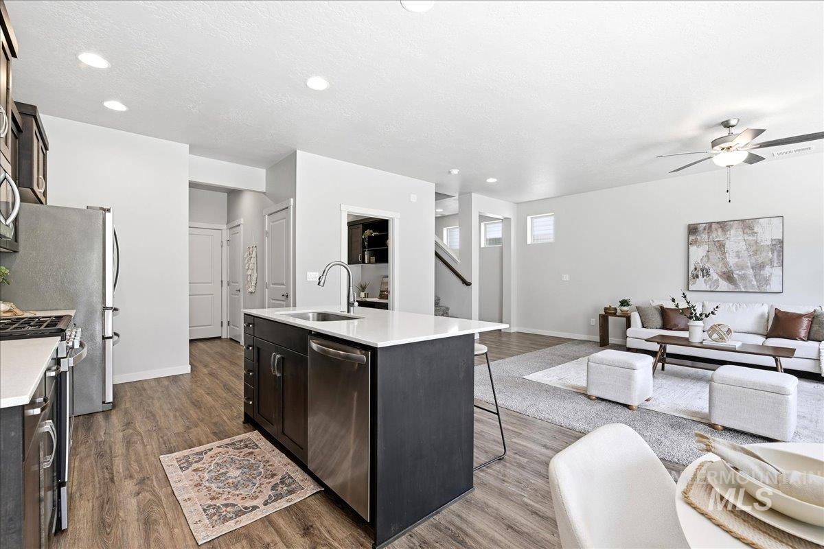 Open-concept living space featuring wood-finish flooring, a kitchen island with a stainless steel sink, and recessed lighting