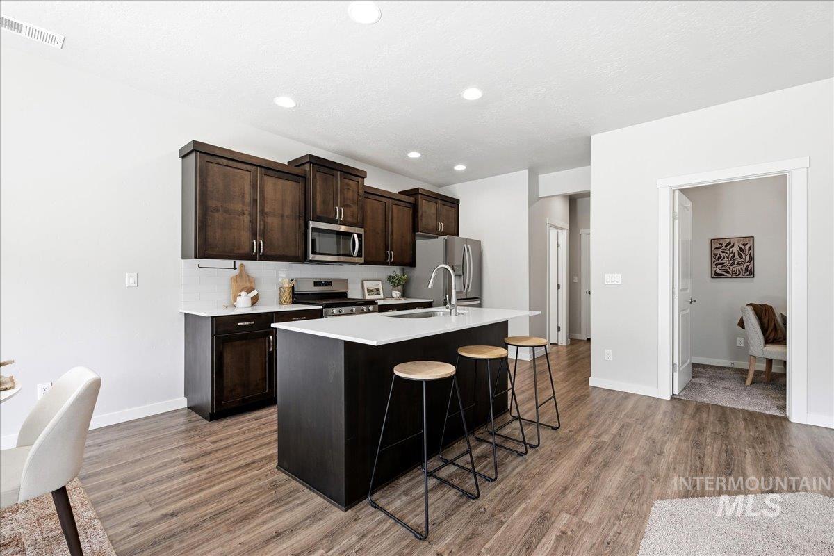 Kitchen featuring a dark wood island with light countertop, dark wood cabinetry, white subway tile backsplash, stainless steel appliances, and wood-finish flooring