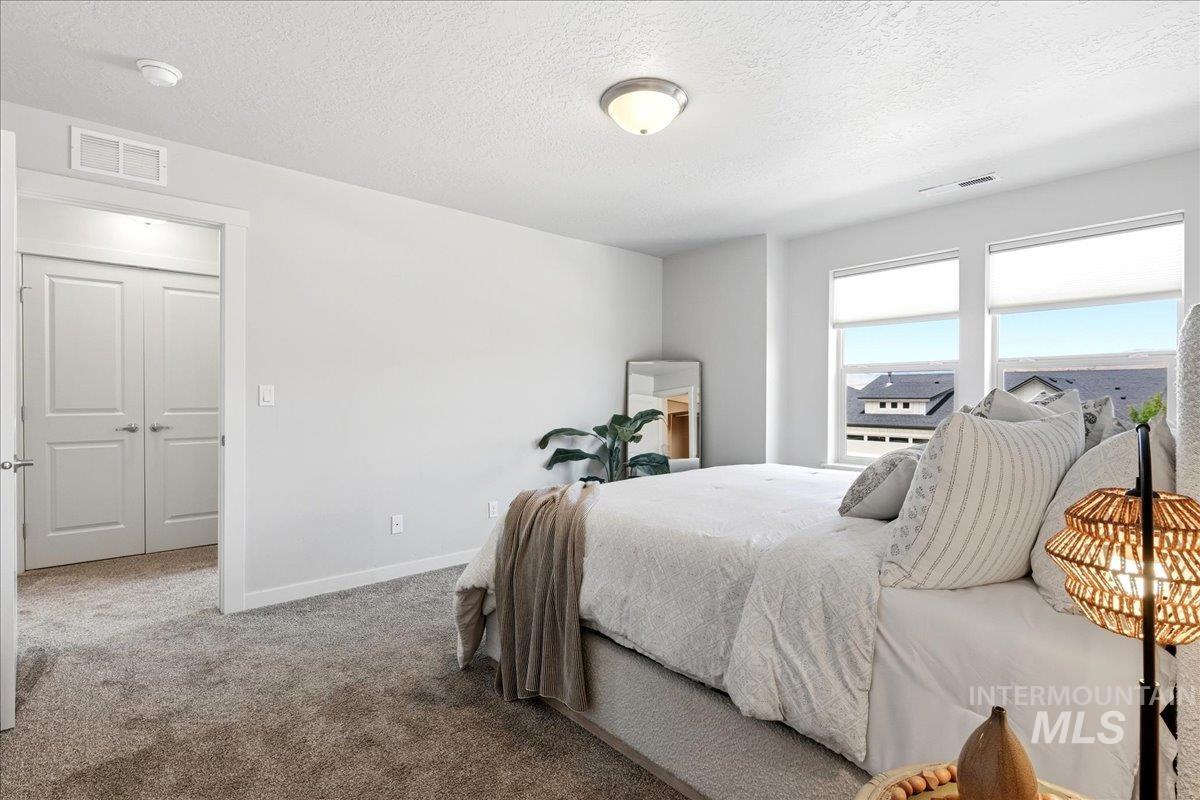 Spacious room featuring multiple windows with roller shades, neutral tone carpeting, and a double-door closet