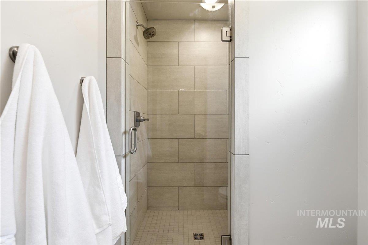 Walk-in shower featuring light-toned rectangular wall tiles, a mosaic tile floor, clear glass enclosure, and a brushed nickel shower head and controls