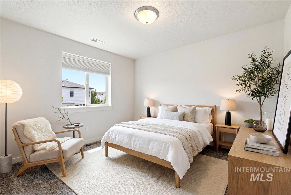 Bright bedroom featuring a large window with roller shades, light wood-finish flooring, a contemporary ceiling light fixture, and white wall finishes