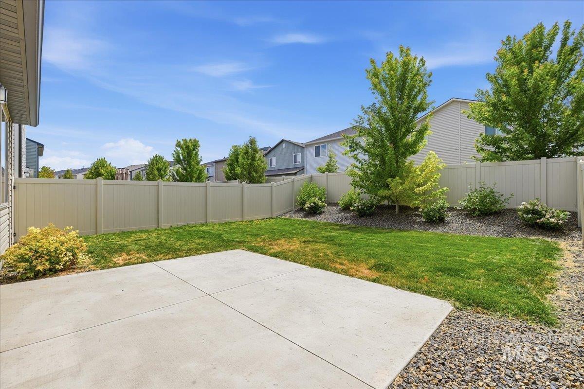 Private backyard space featuring a concrete patio, a section of manicured lawn, and a light-colored privacy fence