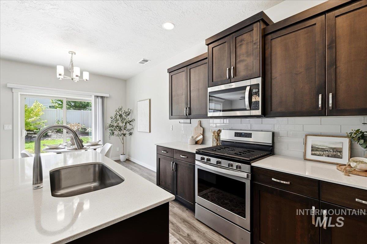 Kitchen featuring dark wood cabinetry, stainless steel appliances, white subway tile backsplash, and light-toned countertops
