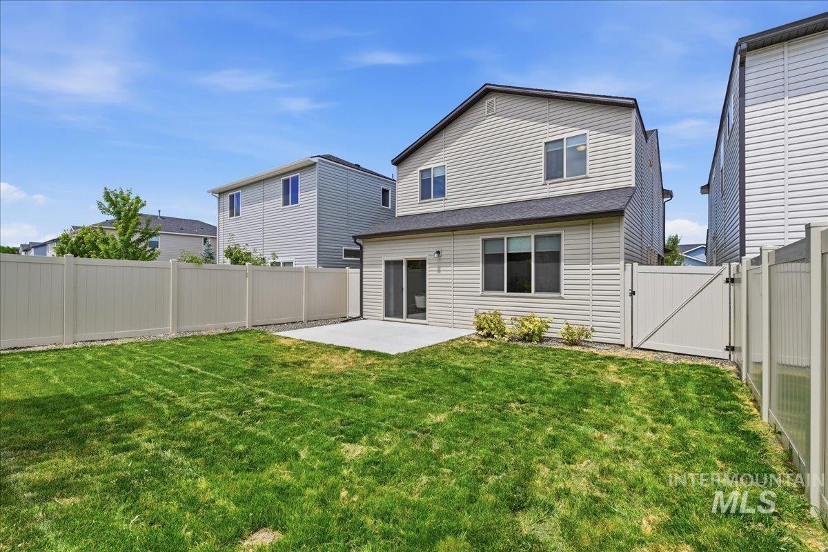 Spacious rear yard featuring an expansive lawn, a concrete patio, and a full-height perimeter fence with a gate