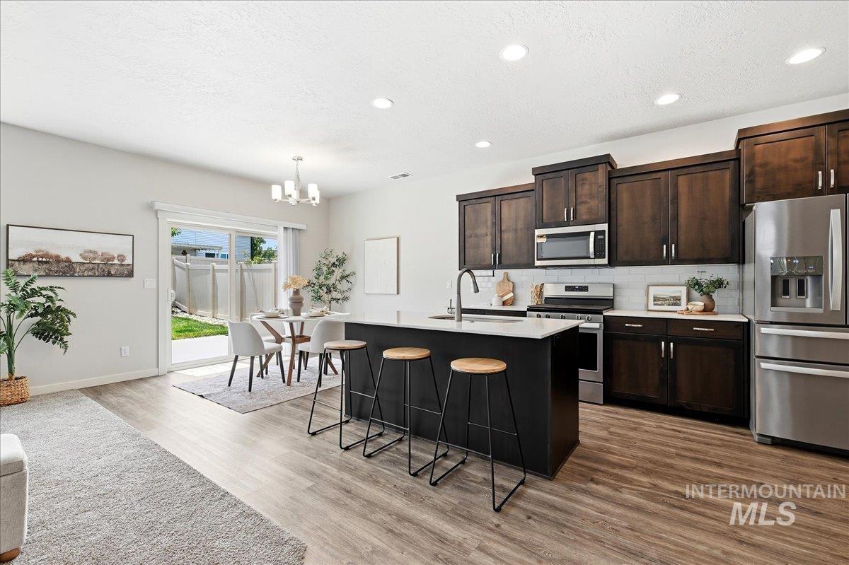 Modern kitchen featuring wood-finish flooring, stainless steel appliances, dark wood cabinetry, white countertops, and a subway tile backsplash