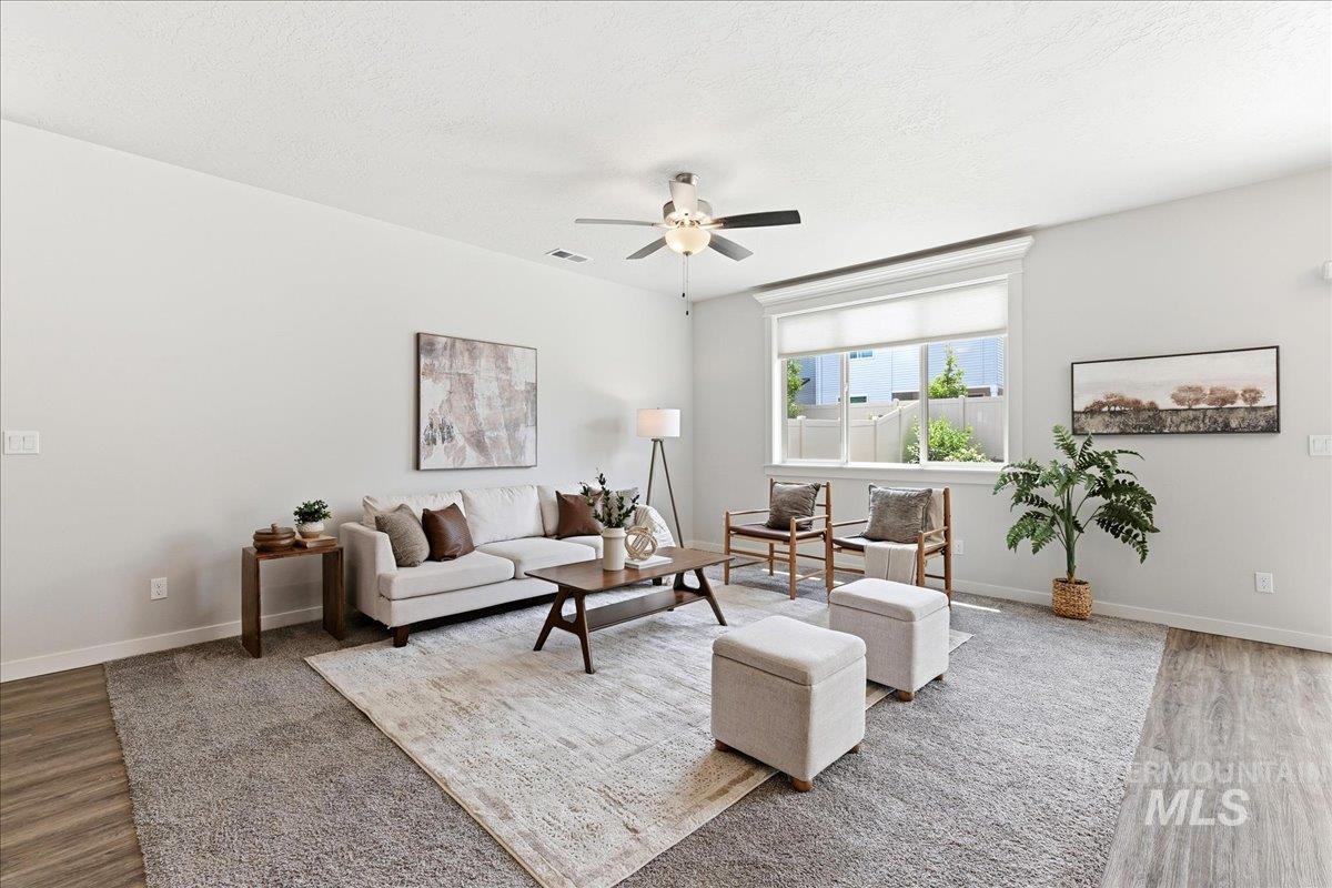 Spacious room featuring light-toned walls, a large window with white trim, wood-finish flooring, and a ceiling fan
