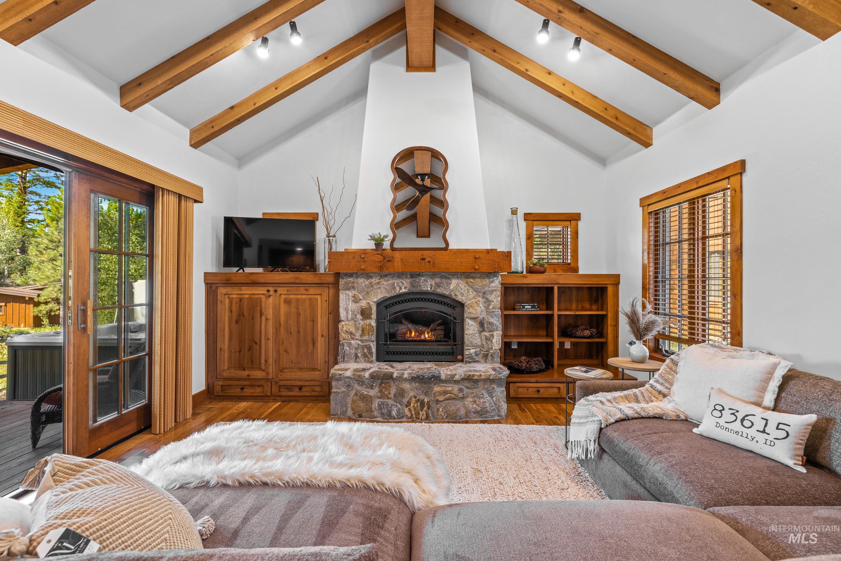 Living room featuring a stone fireplace, beamed ceiling, wood finished floors, high vaulted ceiling, and track lighting