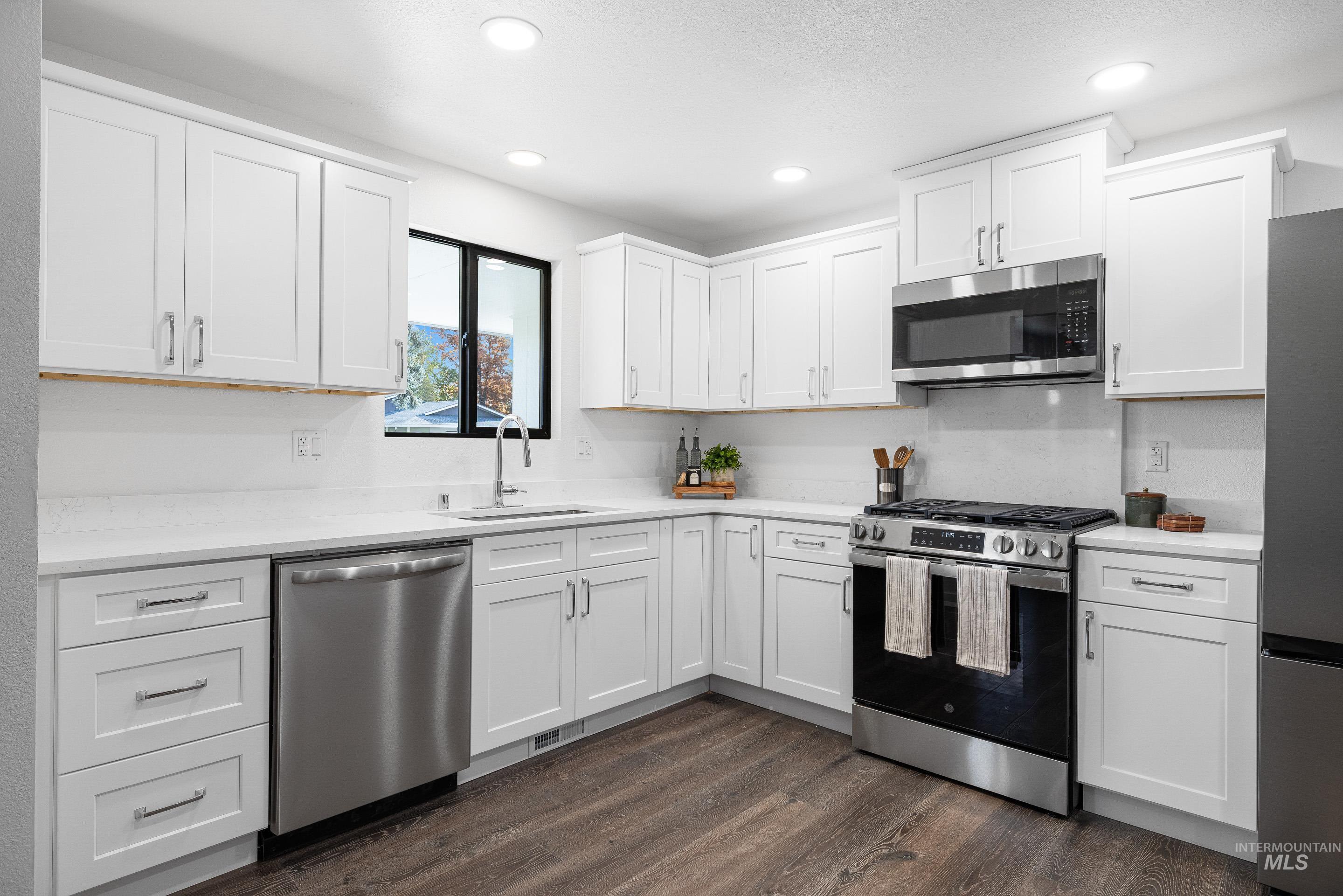 Kitchen featuring appliances with stainless steel finishes, white cabinetry, dark wood-type flooring, recessed lighting, and light stone countertops