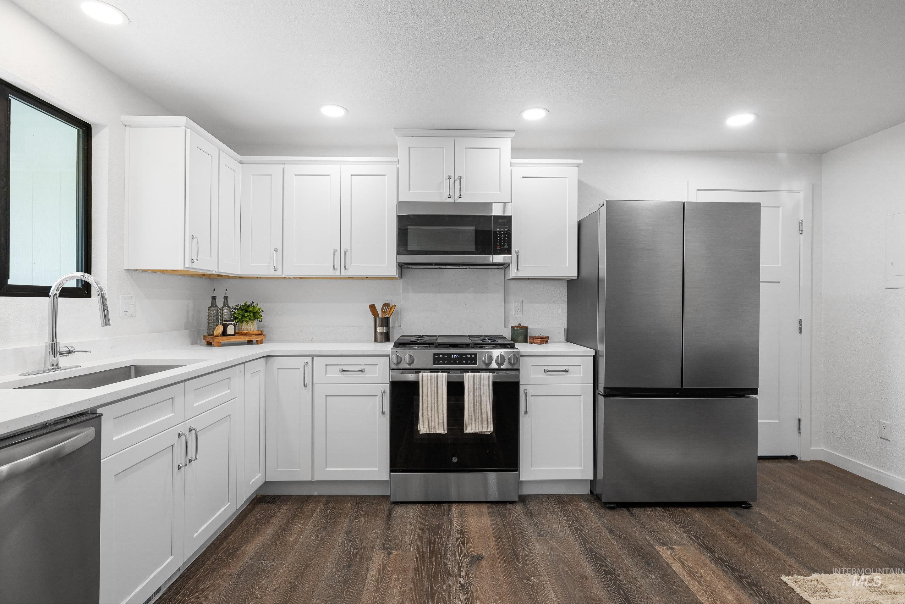 Kitchen with appliances with stainless steel finishes, white cabinets, dark wood-style flooring, recessed lighting, and light stone counters