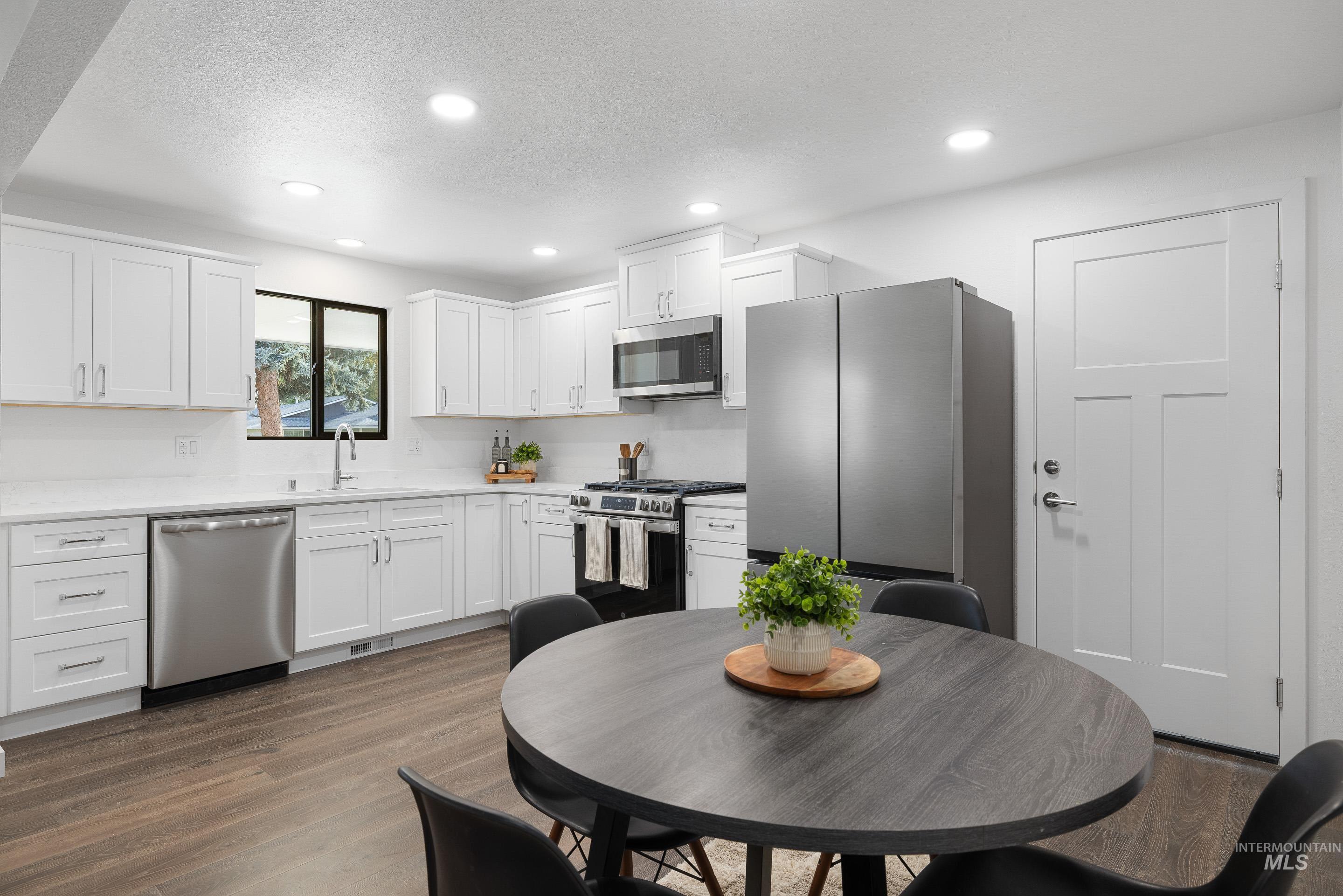 Kitchen with dark wood-style floors, stainless steel appliances, white cabinetry, and recessed lighting