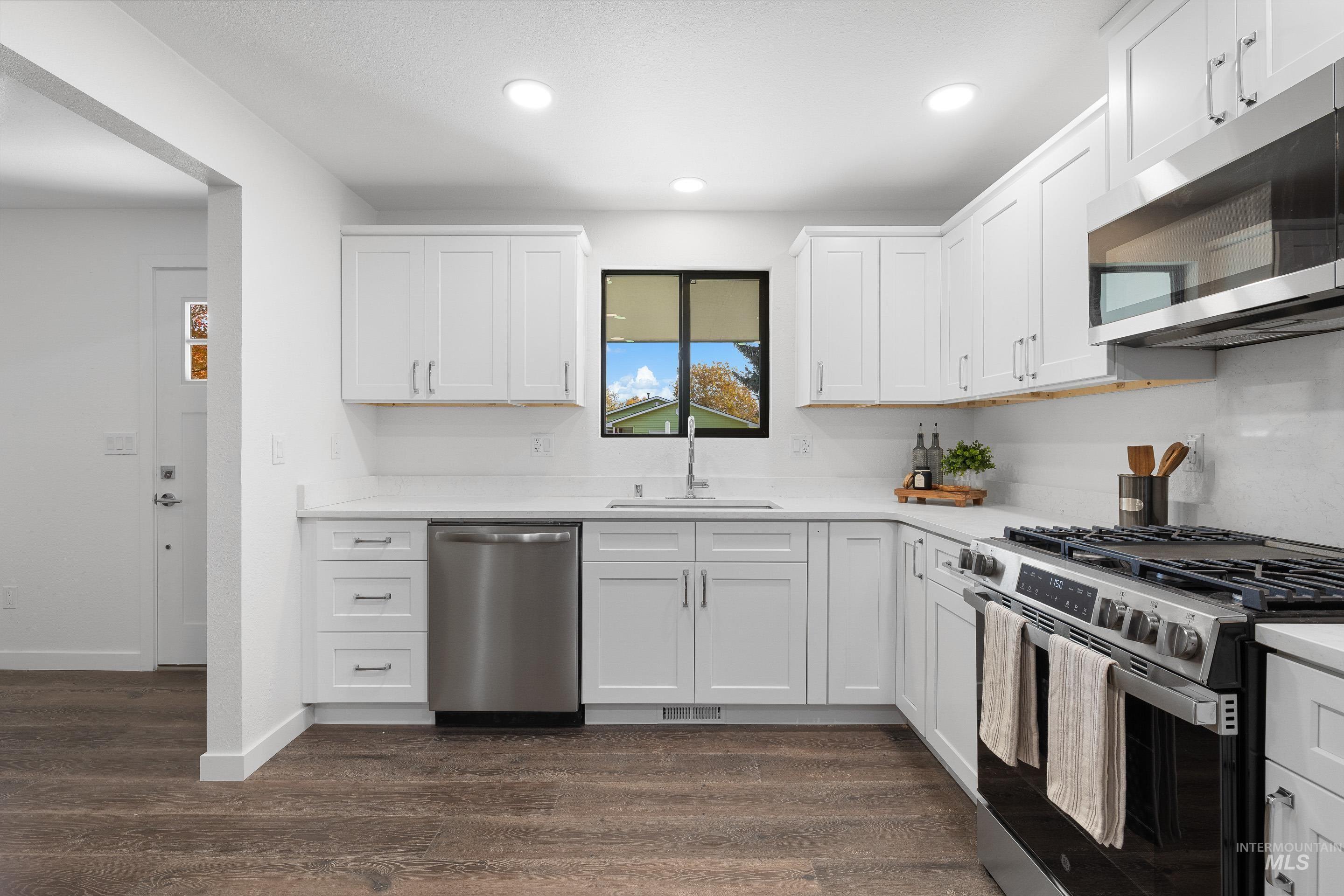 Kitchen with stainless steel appliances, white cabinetry, dark wood-style flooring, recessed lighting, and light stone countertops