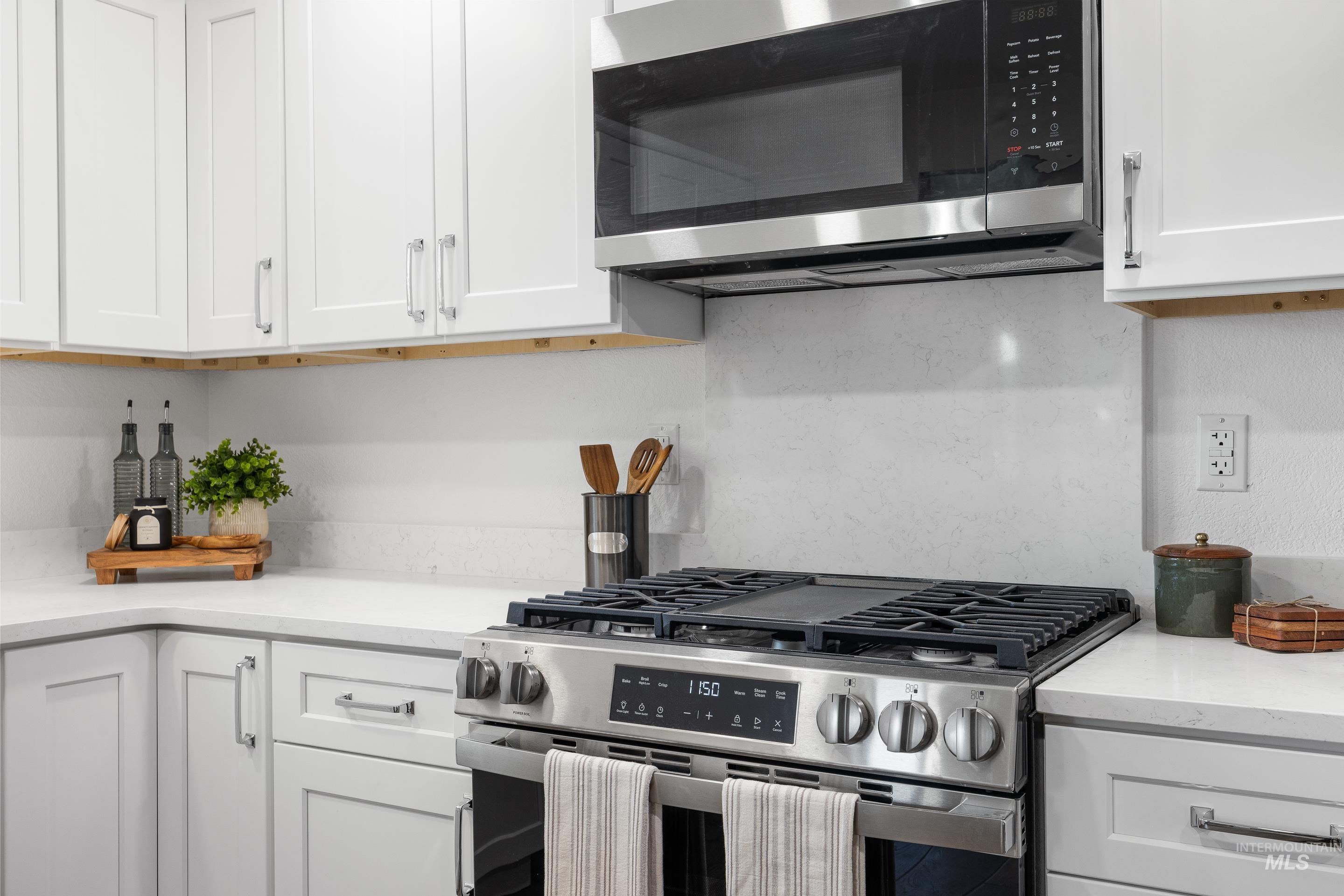 Kitchen featuring stainless steel appliances, white cabinets, and light stone countertops