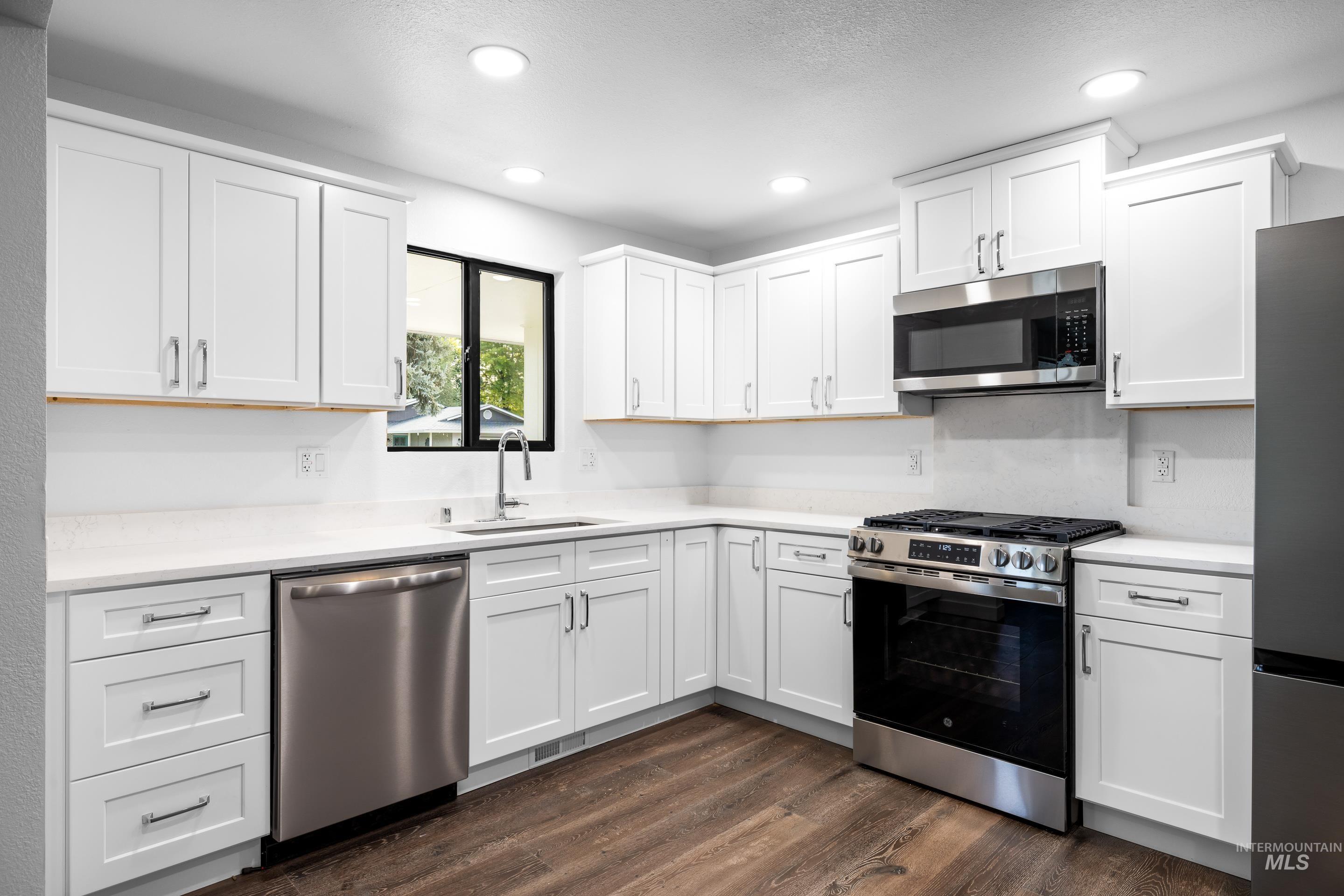 Kitchen featuring appliances with stainless steel finishes, white cabinetry, dark wood-type flooring, recessed lighting, and light stone countertops