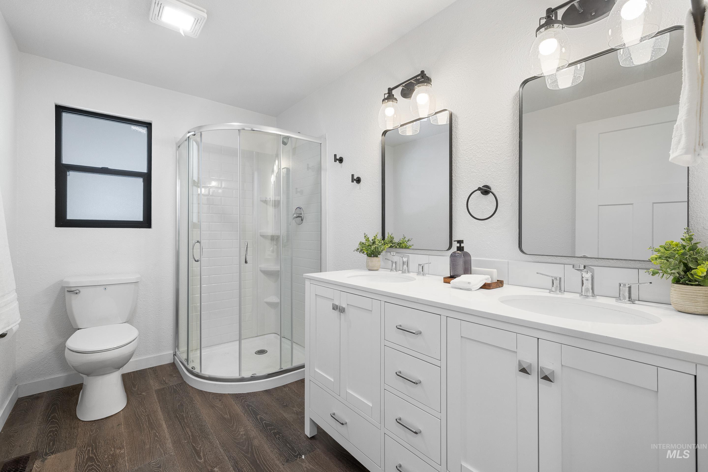 Full bathroom with double vanity, dark wood-style floors, and a stall shower