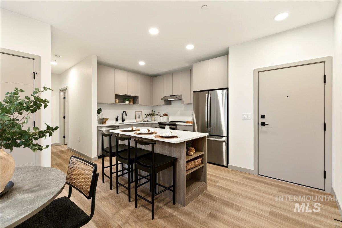 Kitchen with a breakfast bar area, a kitchen island, freestanding refrigerator, light wood-style flooring, and gray cabinets