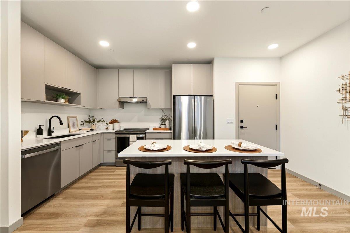 Kitchen featuring gray cabinets, a kitchen breakfast bar, a center island, stainless steel appliances, and light wood-type flooring
