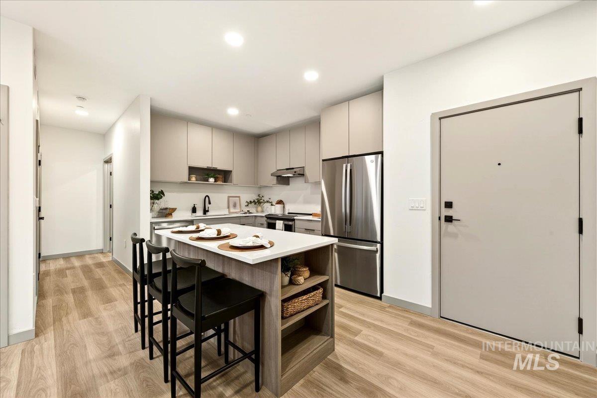 Kitchen with open shelves, a kitchen island, a kitchen breakfast bar, light countertops, and stainless steel appliances