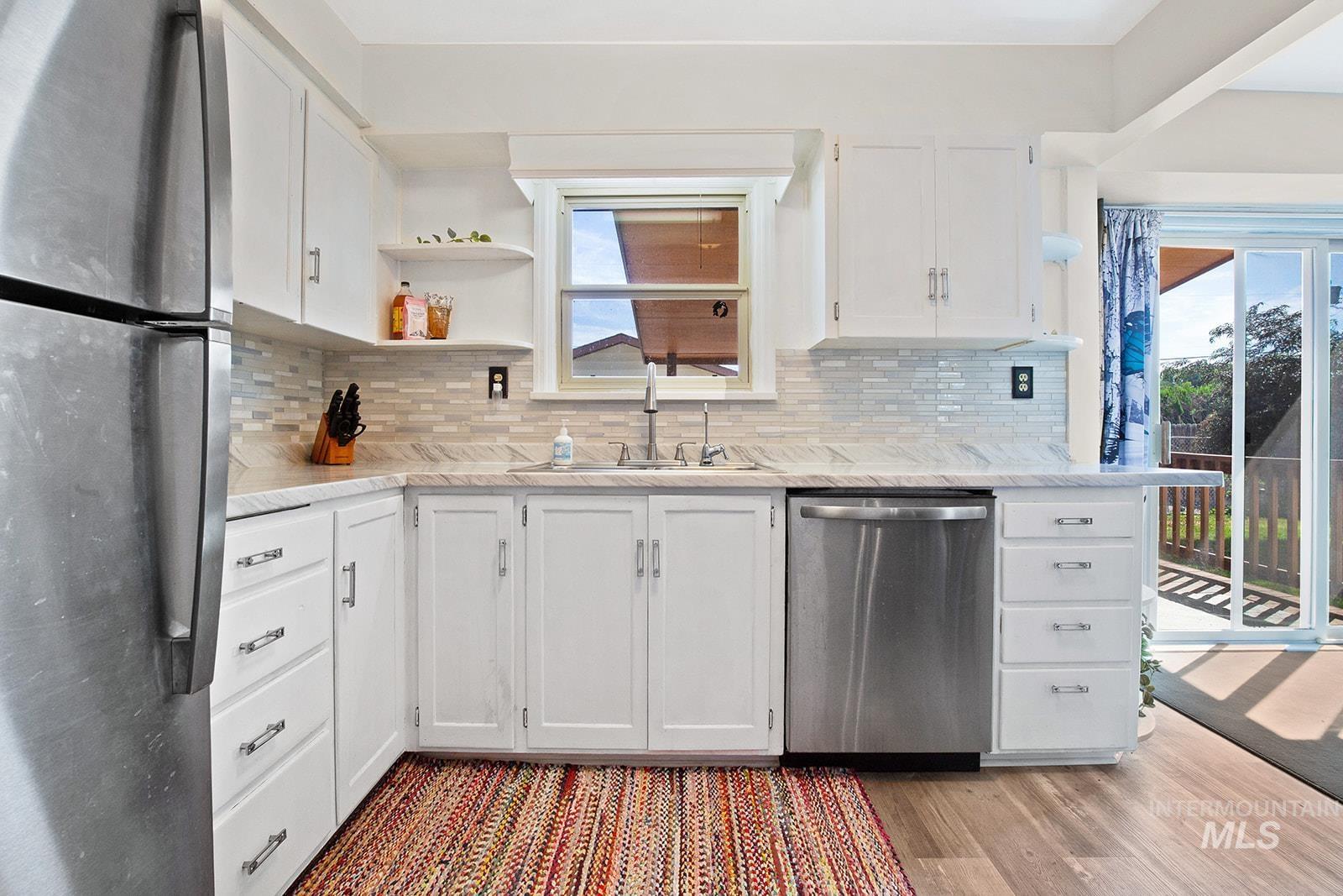 Kitchen featuring stainless steel appliances, open shelves, white cabinets, backsplash, and light wood-style floors