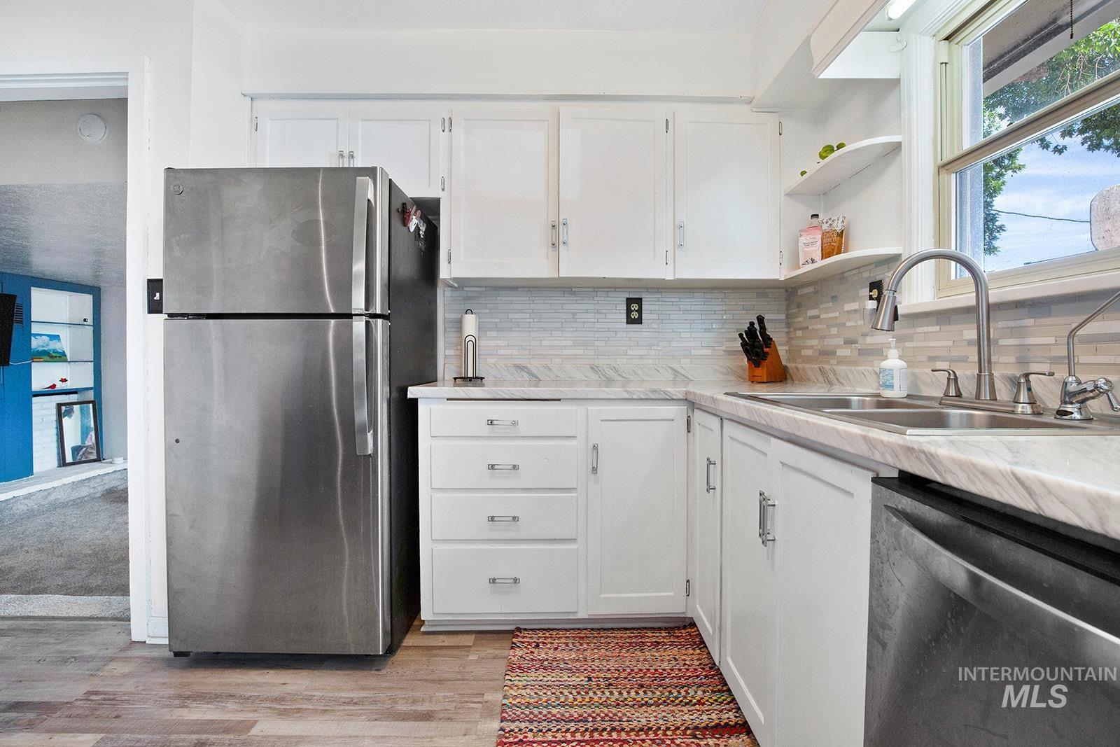 Kitchen with white cabinets, appliances with stainless steel finishes, open shelves, and backsplash