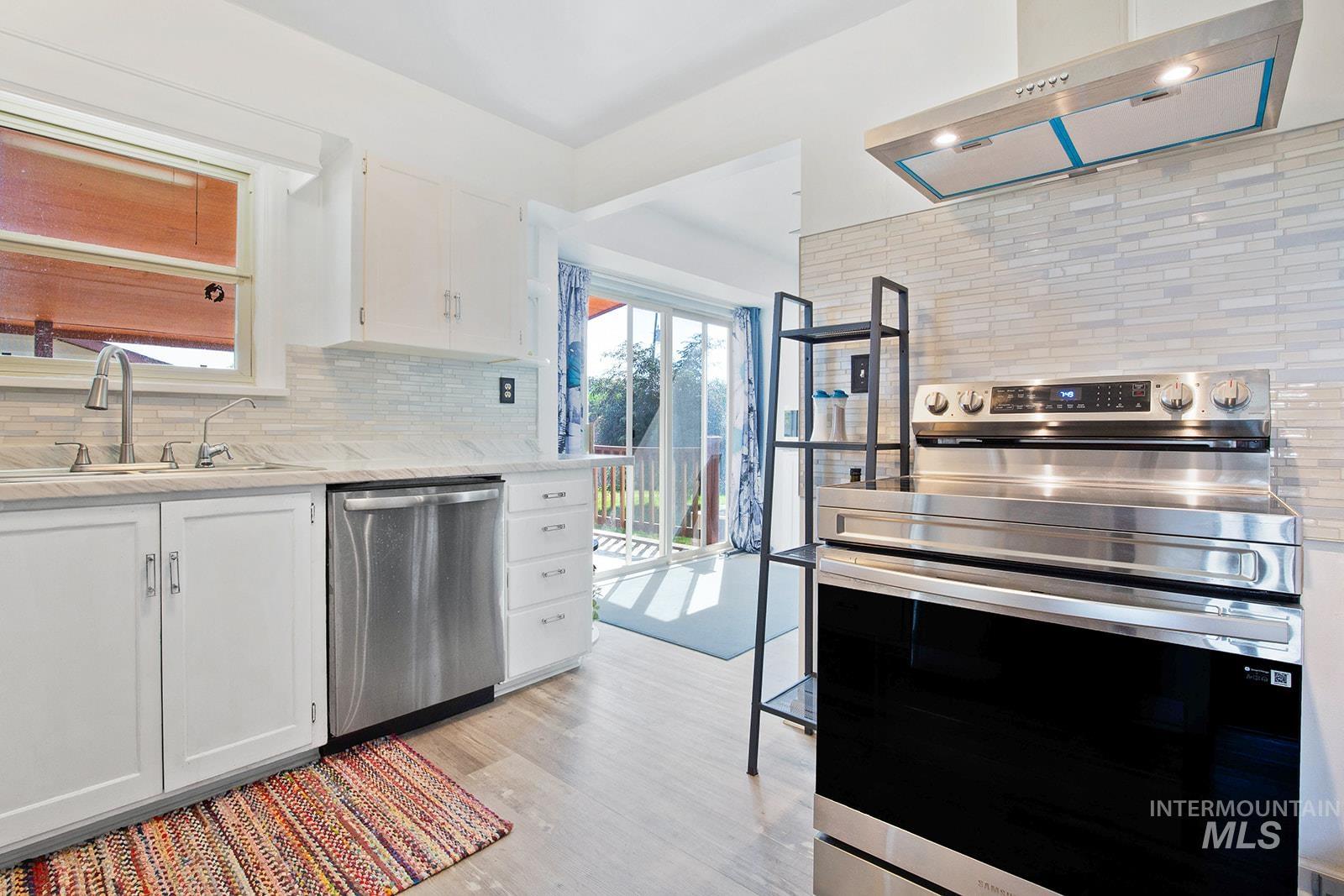 Kitchen with decorative backsplash, stainless steel appliances, under cabinet range hood, white cabinetry, and light wood-type flooring