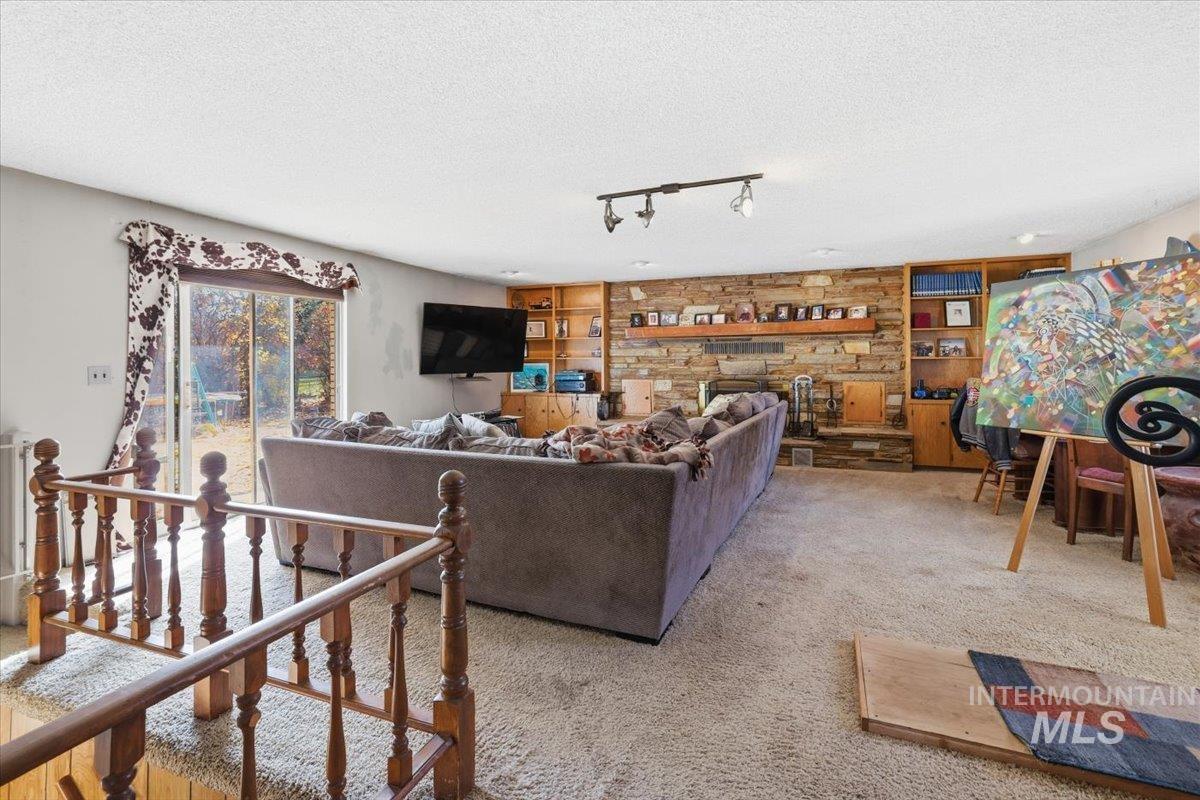 Carpeted living room with a textured ceiling, rail lighting, and a stone fireplace
