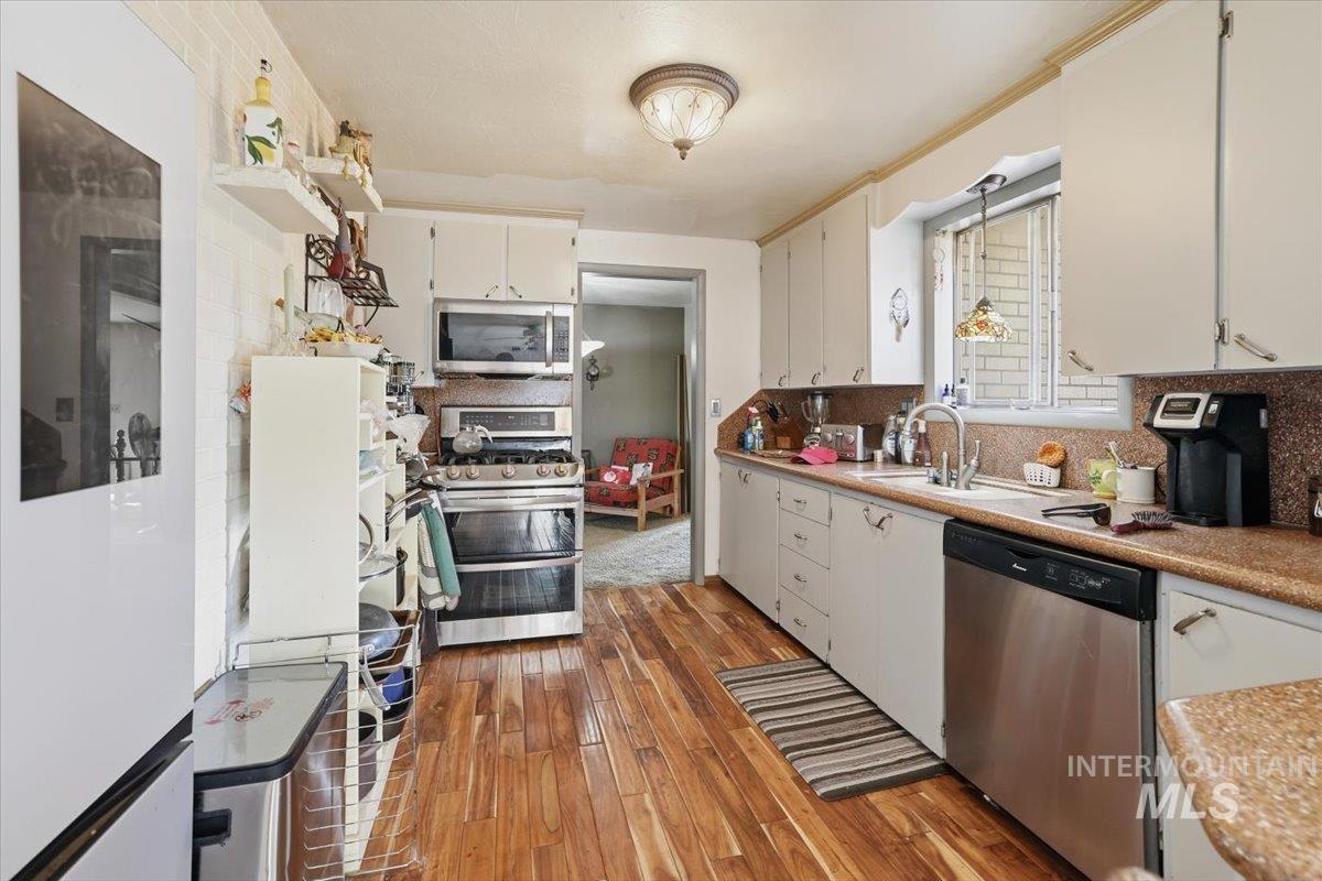 Kitchen featuring decorative backsplash, appliances with stainless steel finishes, light countertops, dark wood-type flooring, and white cabinets