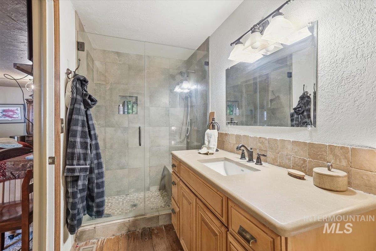Full bathroom with vanity, a stall shower, decorative backsplash, a textured wall, and ensuite bathroom