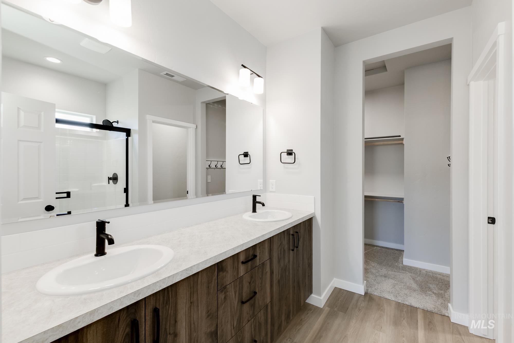Full bathroom with double vanity, a shower stall, a walk in closet, and light wood-style flooring