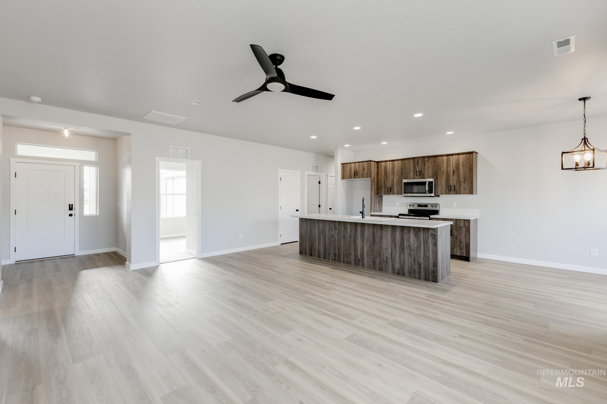 Kitchen with open floor plan, ceiling fan, an island with sink, stainless steel appliances, and light wood-style floors