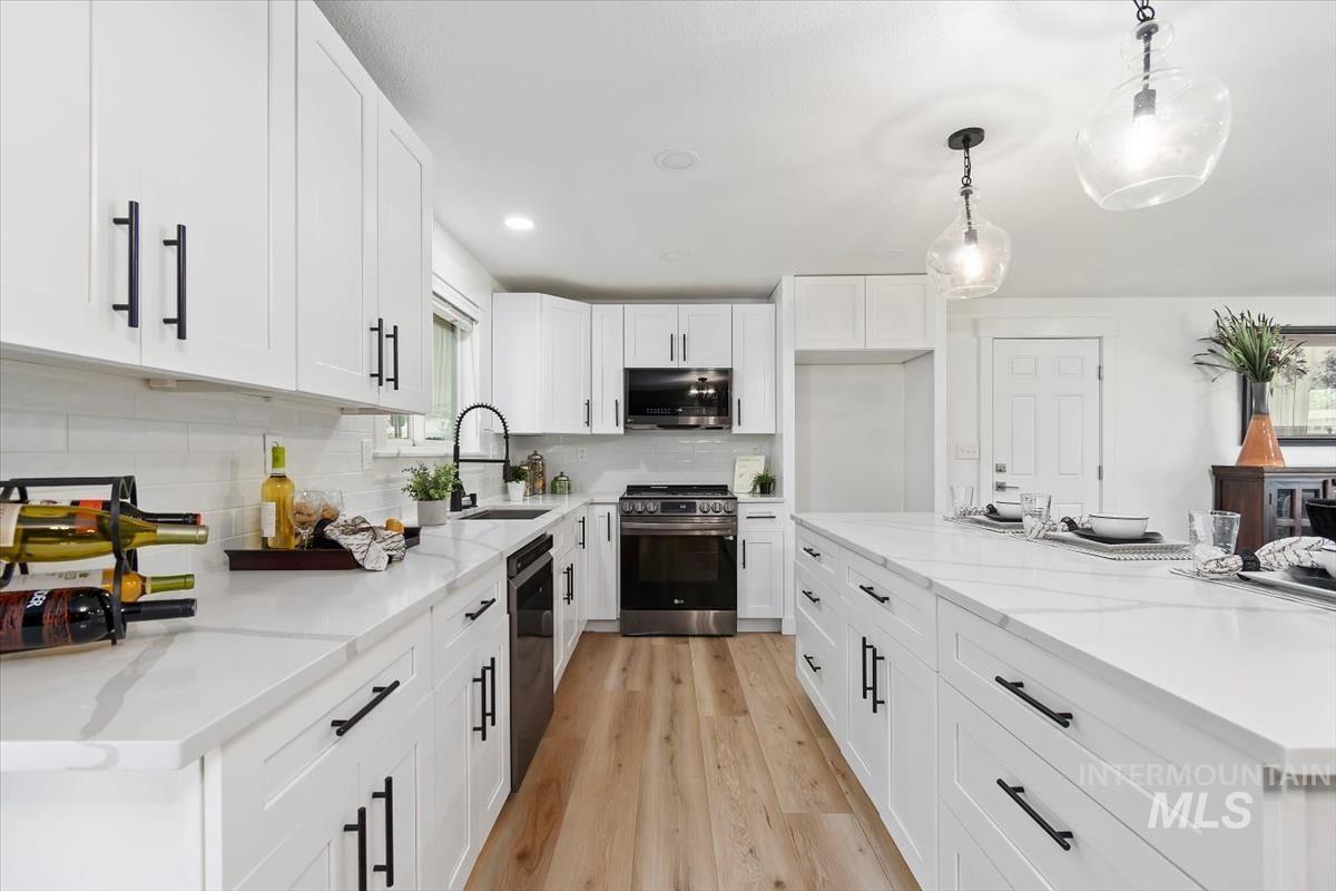 Kitchen with stainless steel appliances, light wood-type flooring, decorative backsplash, recessed lighting, and white cabinetry