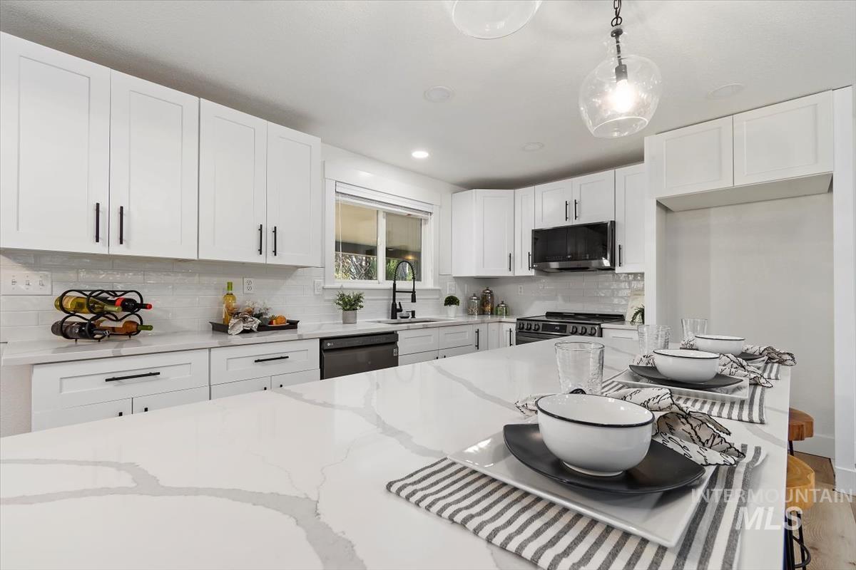 Kitchen with stainless steel stove, black dishwasher, a breakfast bar area, tasteful backsplash, and light stone countertops