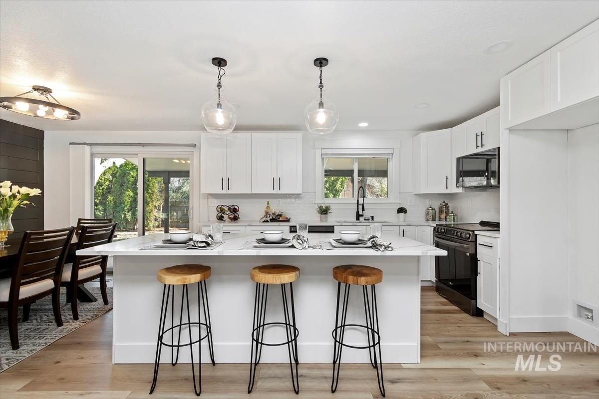 Kitchen featuring electric range oven, black microwave, a breakfast bar area, and a center island