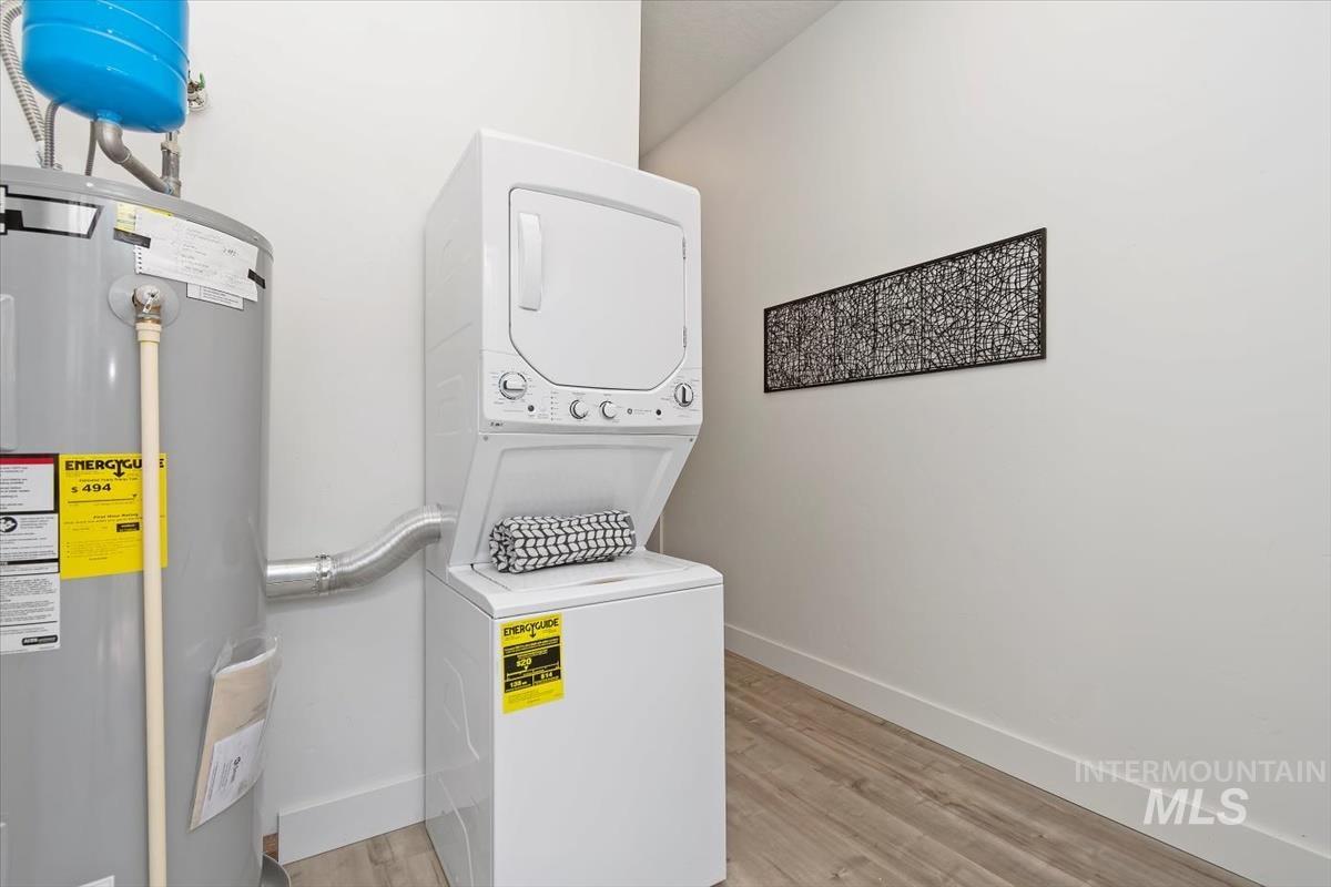 Washroom featuring water heater, stacked washer and clothes dryer, and light wood finished floors
