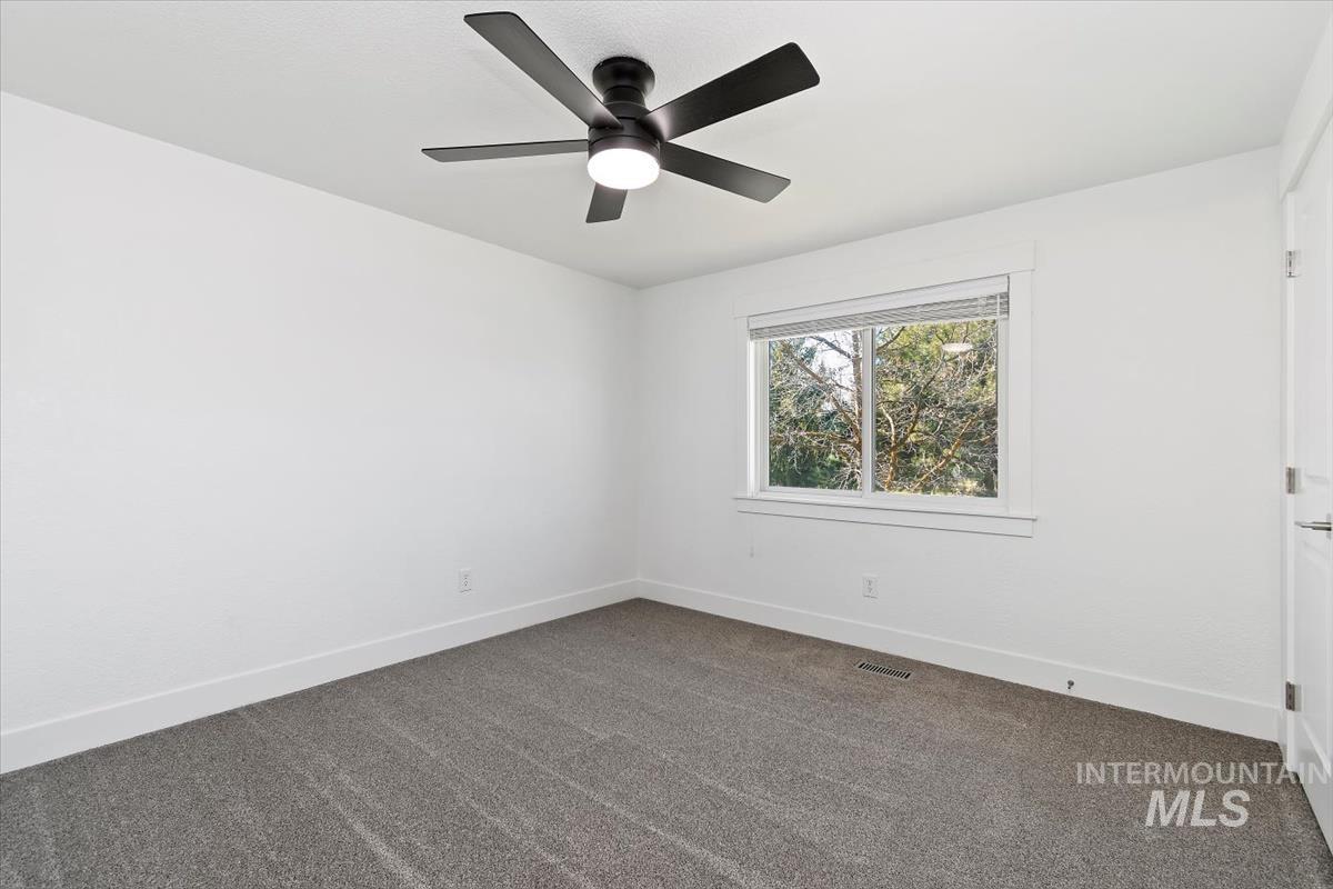 Spare room with a ceiling fan and dark colored carpet