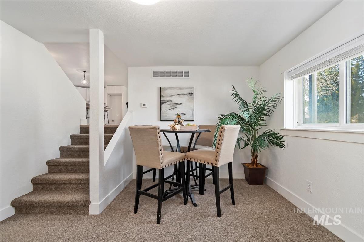 Carpeted dining area with plenty of natural light and stairway