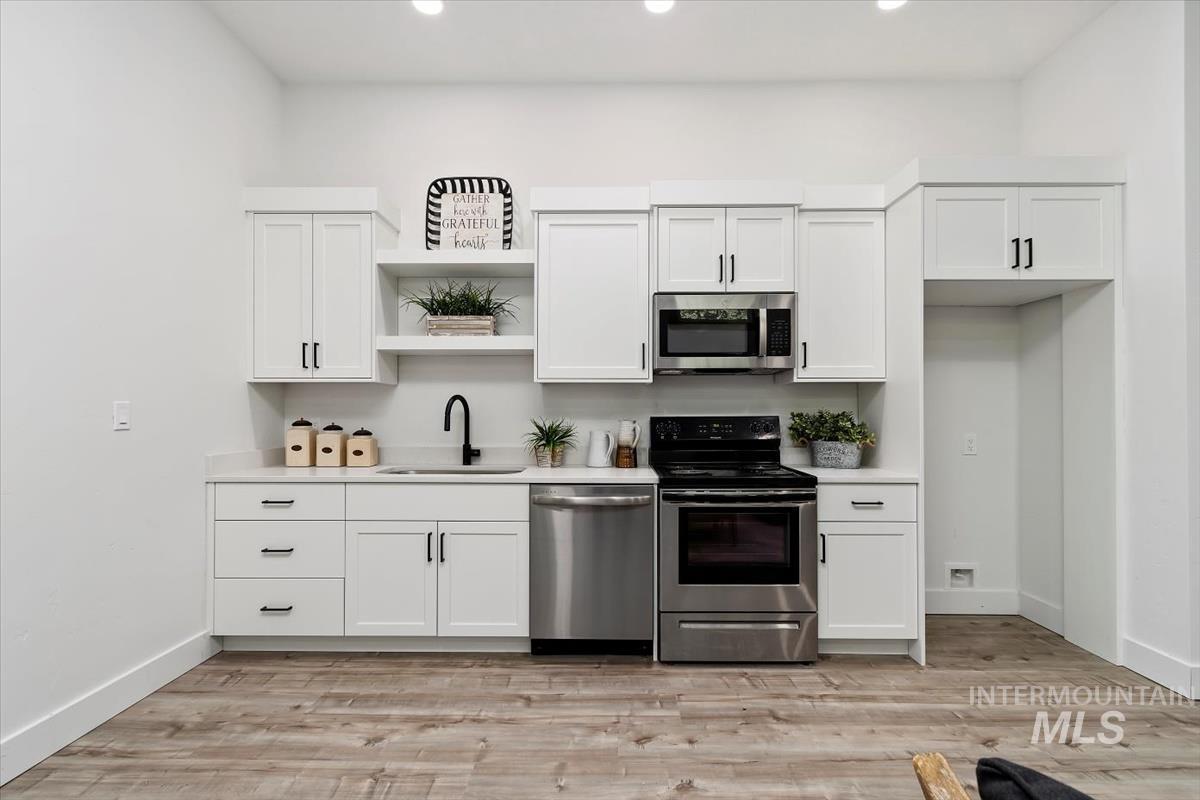 Kitchen featuring appliances with stainless steel finishes, open shelves, light countertops, white cabinets, and recessed lighting