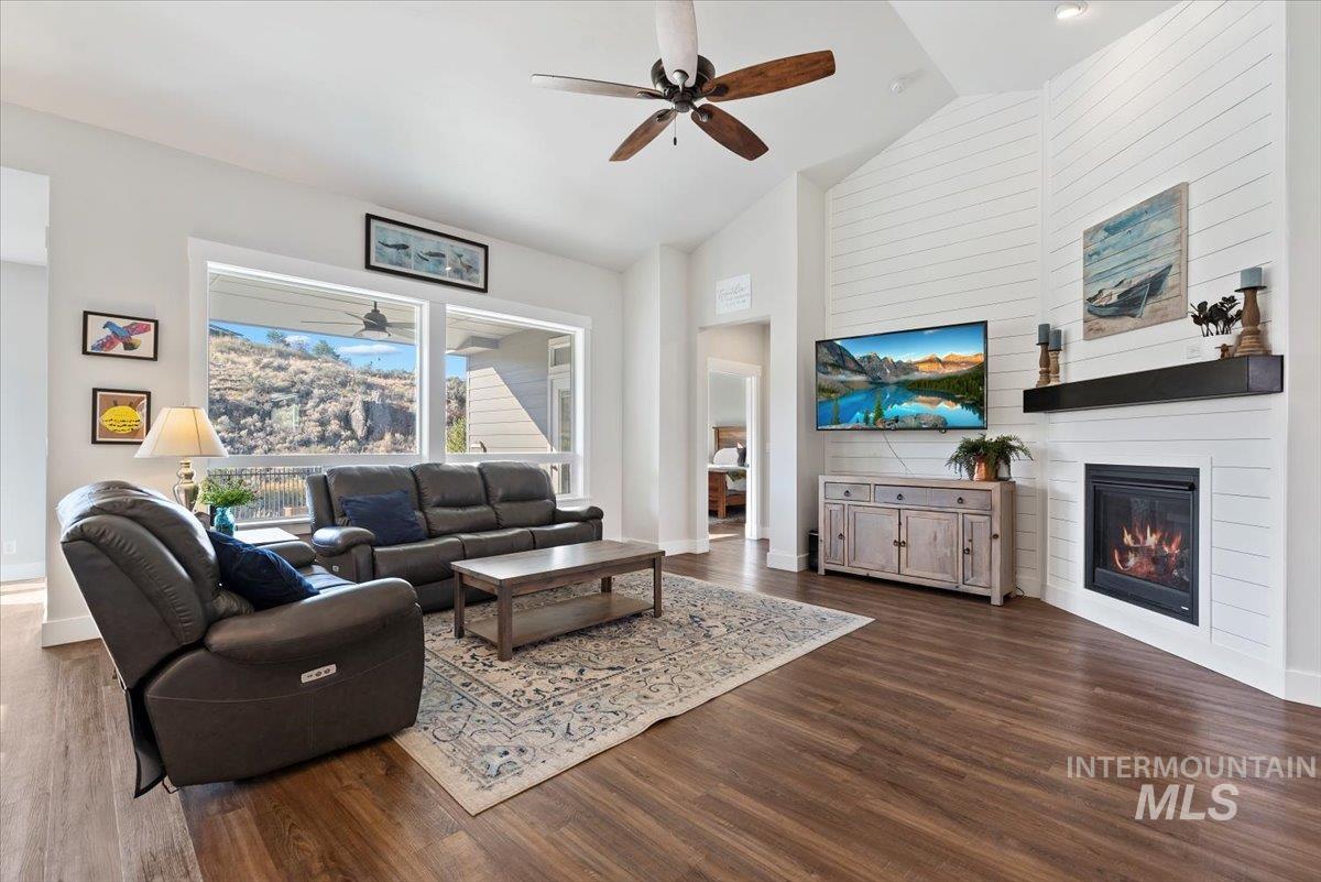 Living room with ceiling fan, high vaulted ceiling, dark wood-style flooring, and a large fireplace