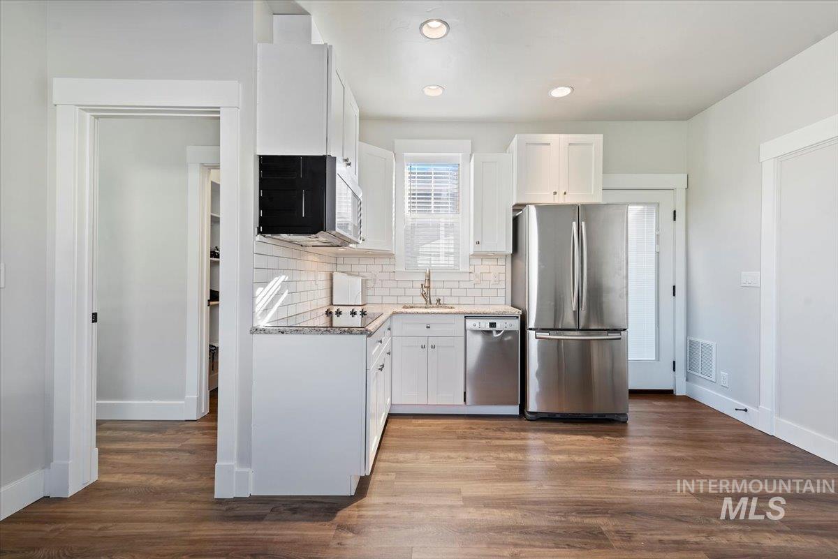 Kitchen with white cabinets, appliances with stainless steel finishes, tasteful backsplash, dark wood-style flooring, and recessed lighting