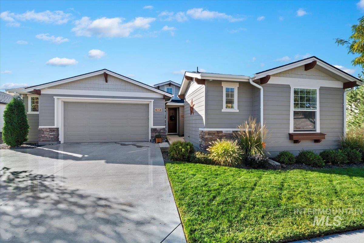 View of front of house featuring driveway, stone siding, a garage, and a front lawn