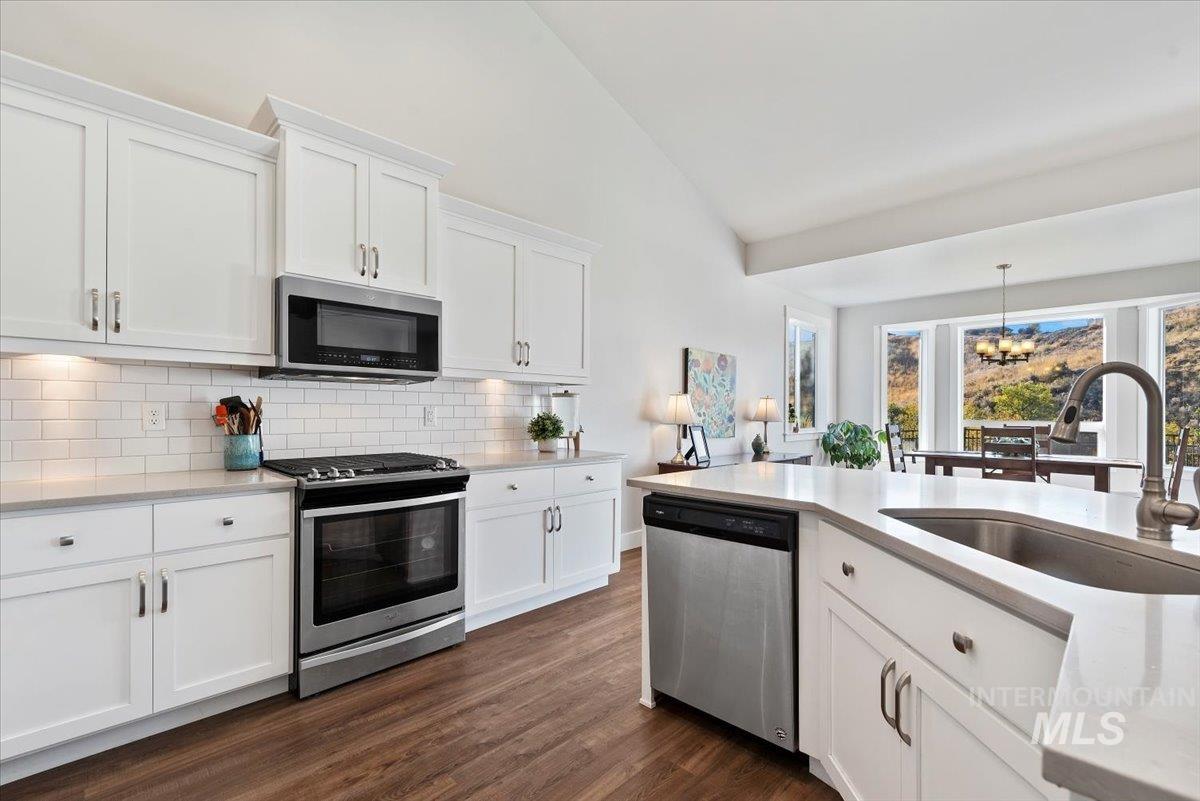 Kitchen featuring white cabinets, appliances with stainless steel finishes, a chandelier, decorative backsplash, and light stone countertops