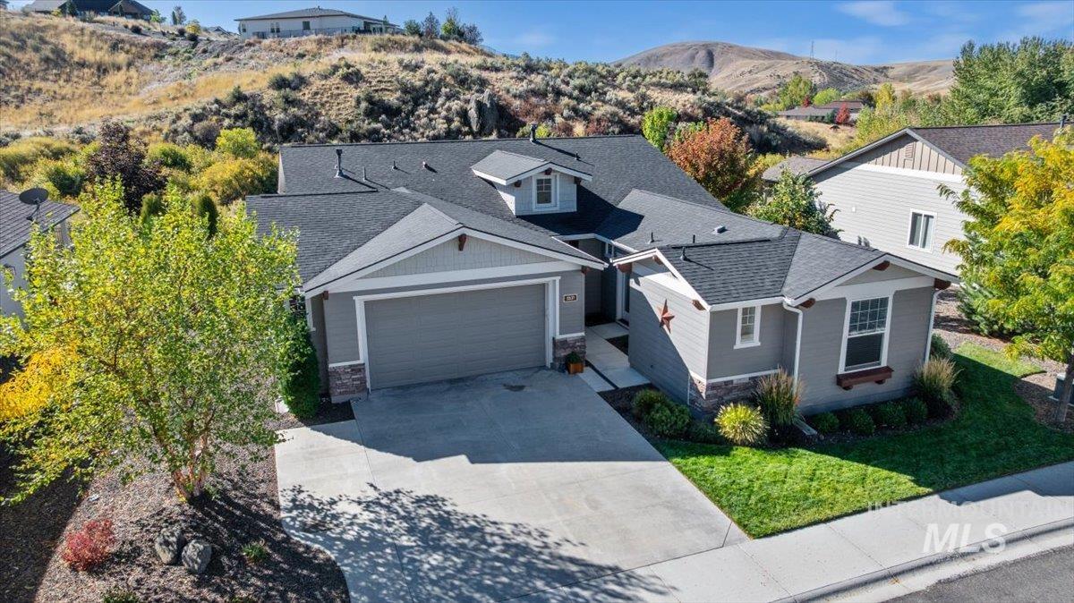 View of front of property featuring stone siding, roof with shingles, driveway, and an attached garage