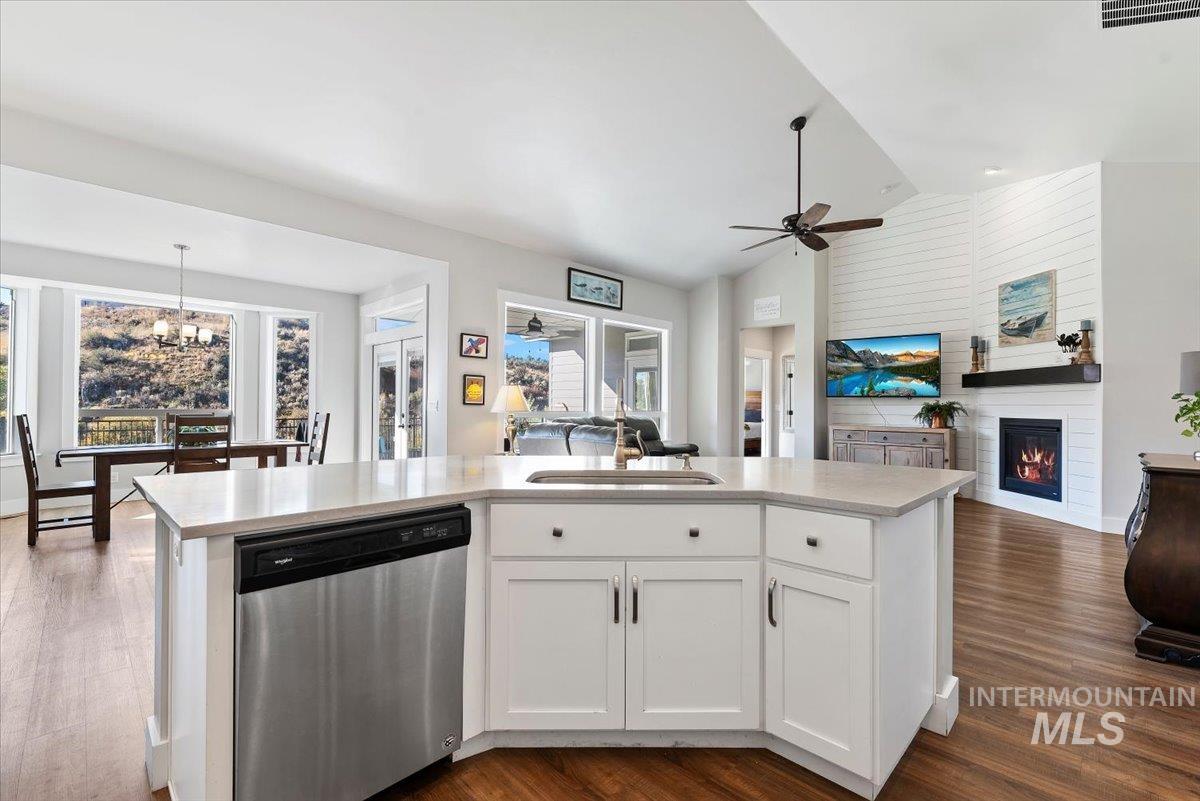Kitchen with open floor plan, an island with sink, stainless steel dishwasher, vaulted ceiling, and white cabinets