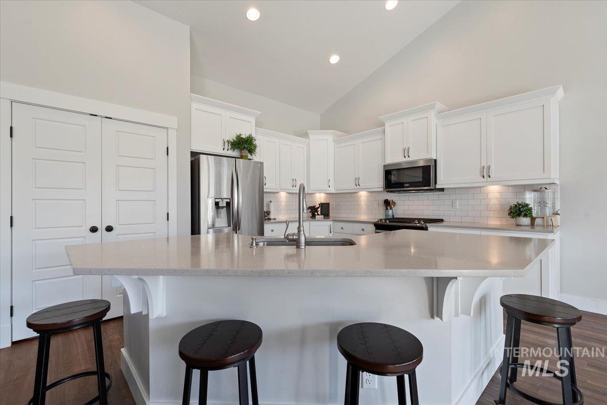 Kitchen with white cabinetry, a kitchen bar, appliances with stainless steel finishes, dark wood finished floors, and vaulted ceiling